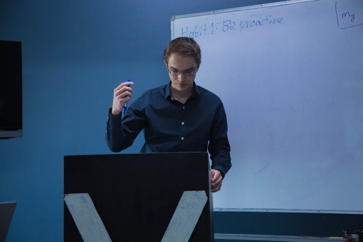 Man with eyeglasses presenting with marker in front of a whiteboard indoors, emphasizing productivity.