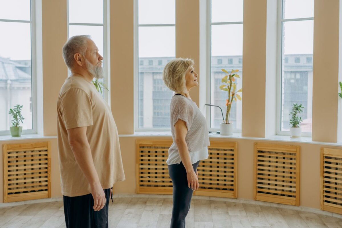 Side view of middle aged serious couple in casual clothes standing in spacious room near windows with potted plants on windowsill in daytime